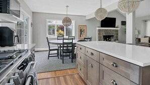 A modern kitchen with a dining area, white cabinetry, and a stone fireplace.