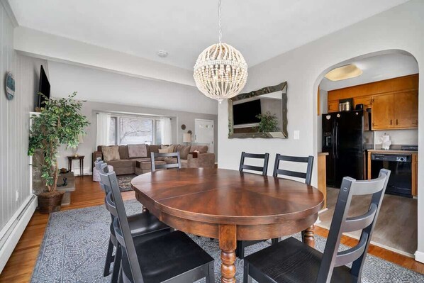 Un coin repas avec une table et des chaises en bois, un lustre et une vue sur la cuisine.