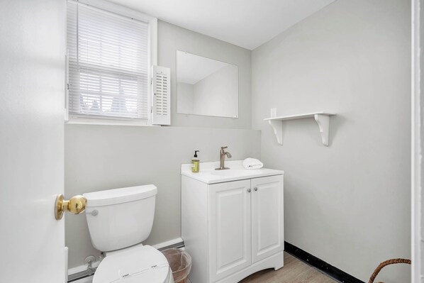 A bathroom with a toilet, a sink, a mirror, and a window with blinds. - Fenwood Coastal Getaway Private Beach Access (Old Saybrook)