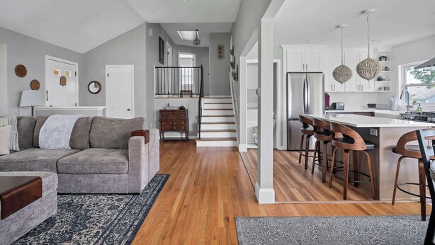 A modern kitchen with a central island, wooden bar stools, and a staircase leading to an upper level.
