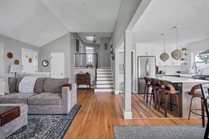 A modern kitchen with a central island, wooden bar stools, and a staircase leading to an upper level. - Fenwood Coastal Getaway Private Beach Access (Old Saybrook)