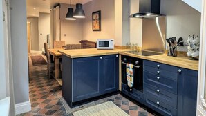 A modern kitchen with dark blue cabinets, a wooden countertop, and a microwave. There are pendant lights above the island and a stove with a colorful towel. - Beautiful apartment in Central London, Paddington (London)
