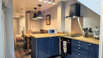 A modern kitchen with dark blue cabinets, a wooden countertop, and a microwave. There are pendant lights above the island and a stove with a colorful towel.