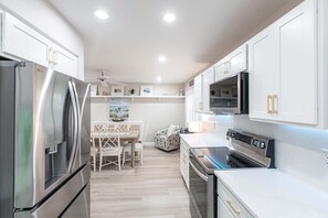 A modern kitchen with white cabinetry, stainless steel appliances, and a dining area with a table and chairs.