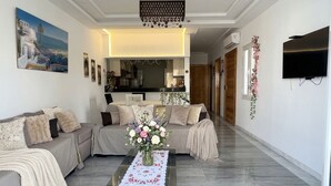 A living room with a sofa, a coffee table with a vase of flowers, a TV, and a painting on the wall. - Chic & cozy apartment with balcony, 2 bathrooms – Carthage, near the airport (Al Karm)