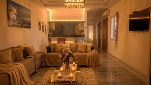 A living room with a sofa, a coffee table with candles, a chandelier, and a TV on the wall. - Chic & cozy apartment with balcony, 2 bathrooms – Carthage, near the airport (Al Karm)