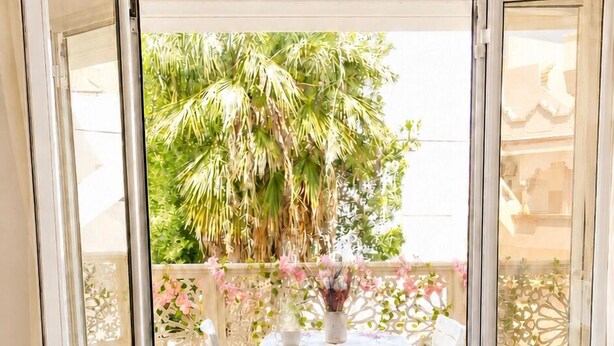 A room with a glass door leading to an outdoor area with a table and chairs, a white tablecloth, and a vase with flowers. - Chic & cozy apartment with balcony, 2 bathrooms – Carthage, near the airport (Al Karm)
