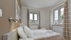 A bedroom with a bed, white curtains, a window, and a wall-mounted light fixture. - Holiday apartment with air conditioning and outdoor pool (Fažana)