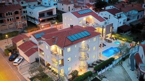 A multi-story hotel with a swimming pool, balconies, and a well-lit entrance.