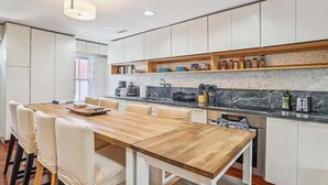 A modern kitchen with white cabinets, a wooden dining table, and a marble backsplash. - Downtown Pinkney House w/Parking (Annapolis)
