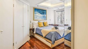 A bedroom with a skylight, a bed with blue bedding, a painting on the wall, and a window with a view of trees. - Downtown Pinkney House w/Parking (Annapolis)