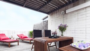 A wooden deck with a table and chairs, a small table with a vase of flowers, and a wall-mounted security camera.