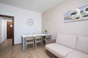 A modern living room with a sofa, a dining table with chairs, a wall clock, and a welcome sign. - Holiday apartment with air conditioning and outdoor pool (Fažana)