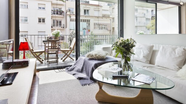 Una sala de estar moderna con una mesa de centro de vidrio, un sofá y un balcón con una lámpara roja.