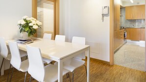 A modern dining area with a white table and chairs, a vase of white flowers, and a wooden-framed window with blinds. - Charming Apartment in the Center w/ Balcony for 6 (Barcelona)