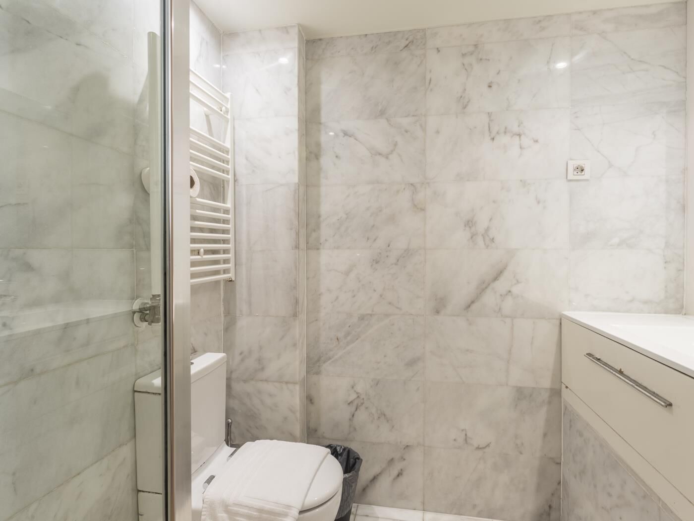 A bathroom with a glass shower enclosure, a toilet, and a sink with a countertop.