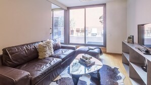 Una sala de estar moderna con un sofá de cuero, una mesa de centro de vidrio y un televisor sobre un mueble.