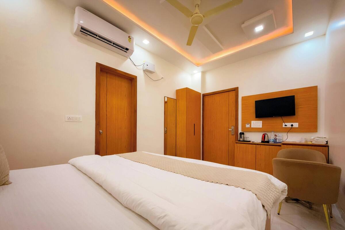 Ein Hotelzimmer mit Bett, Kleiderschrank, Schreibtisch, Stuhl, Fernseher und Deckenventilator.