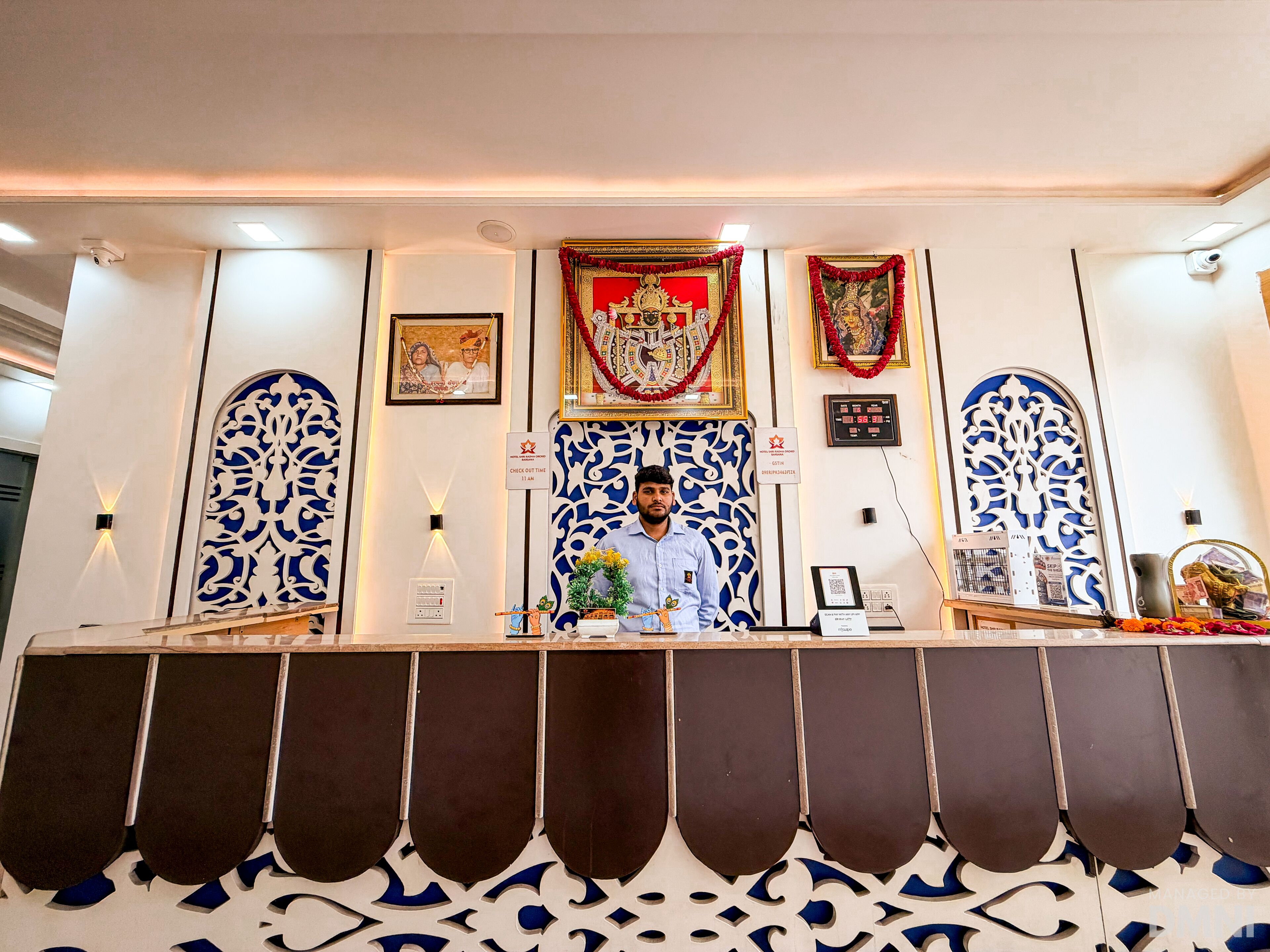 A reception desk with a man standing behind it, a clock, and framed pictures on the wall.