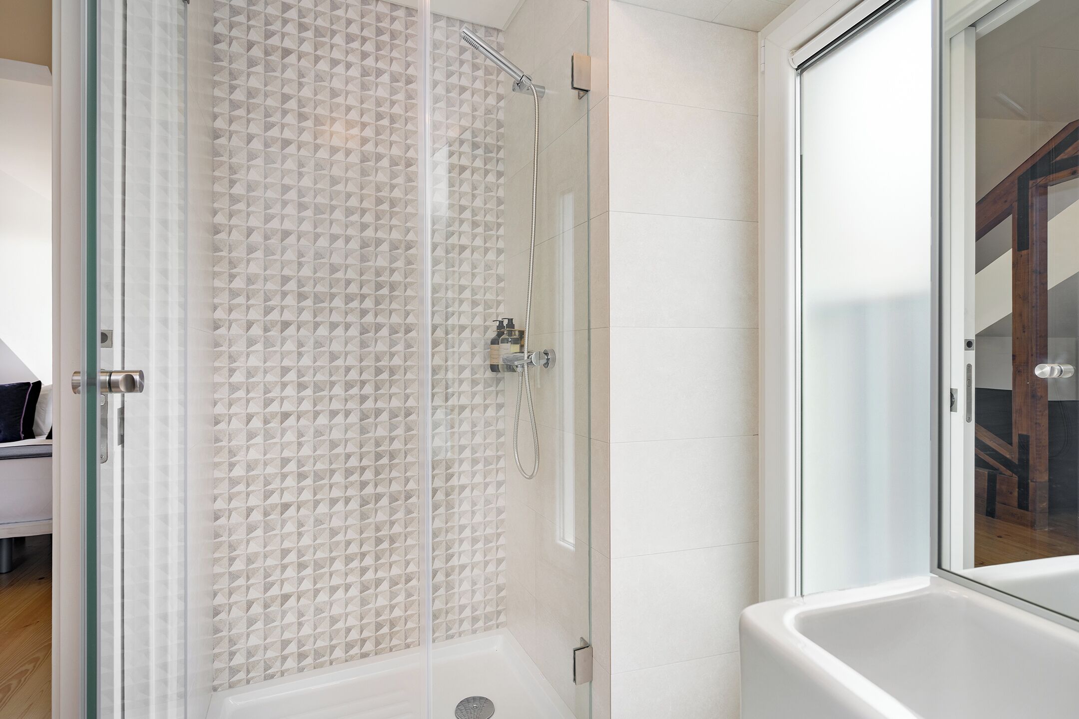 Een moderne badkamer met een douchecabine van glas, een wit bad en een betegelde vloer.