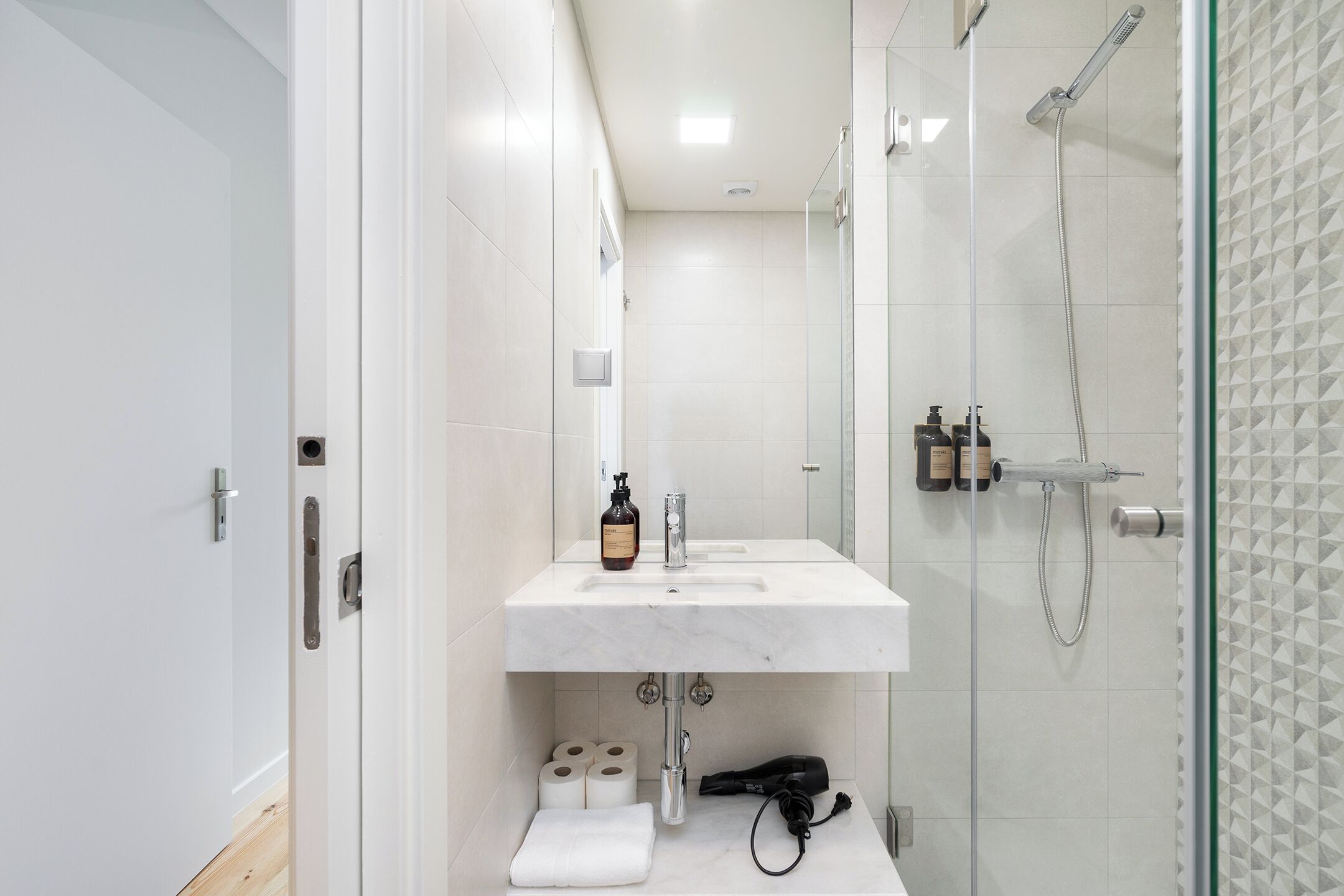 A modern bathroom with a white sink, toilet paper, and a hairdryer.