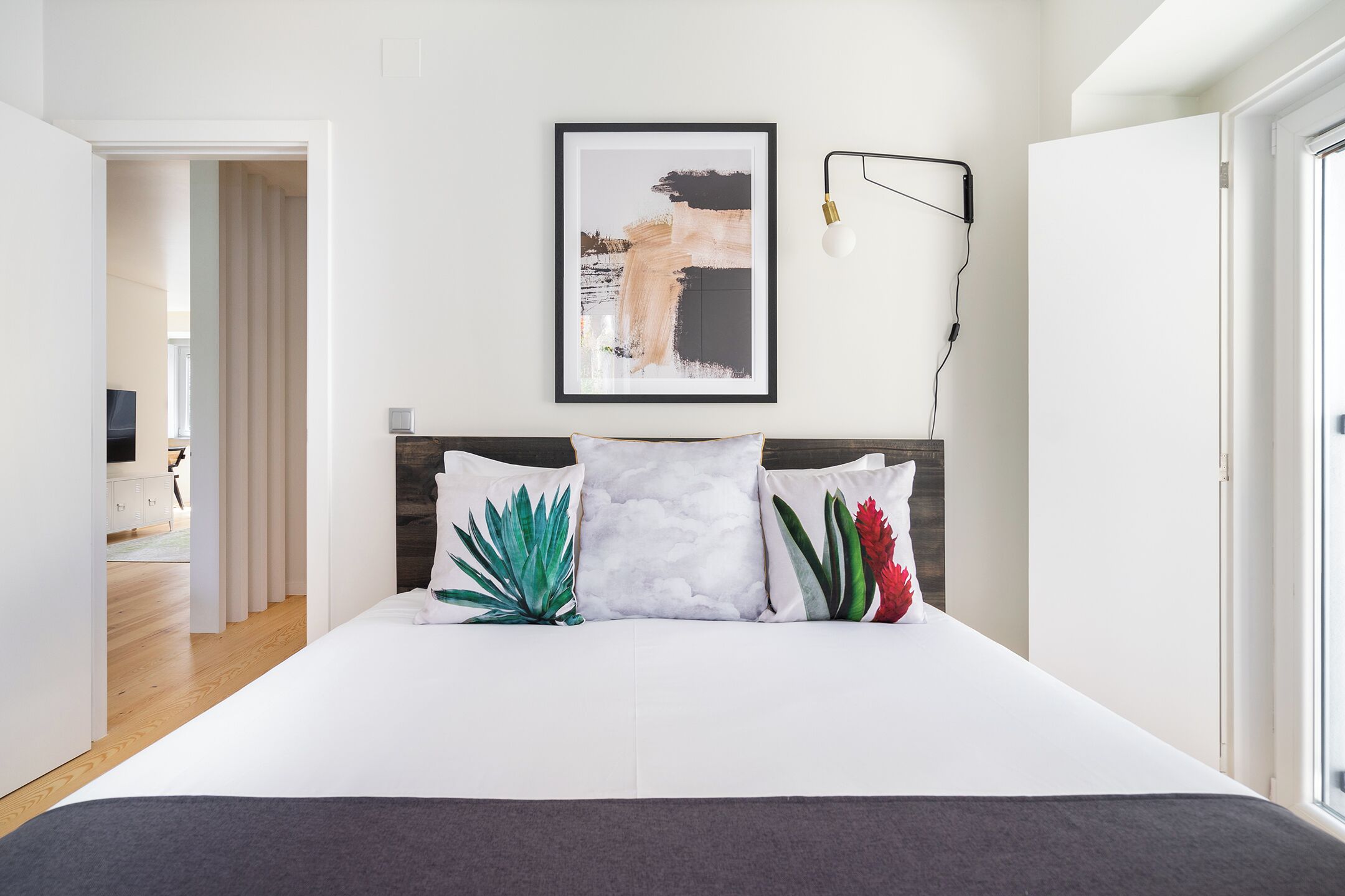 A modern bedroom with a large bed, a framed abstract painting, and a bedside lamp.