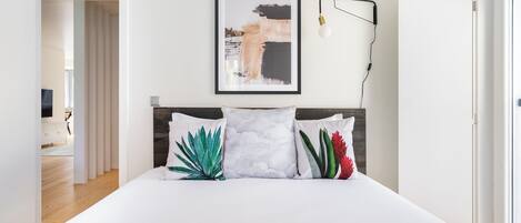 A modern bedroom with a large bed, a framed abstract painting, and a bedside lamp.