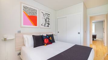 Een moderne hotelkamer met een groot bed, een houten hoofdbord en twee abstracte schilderijen aan de muur.