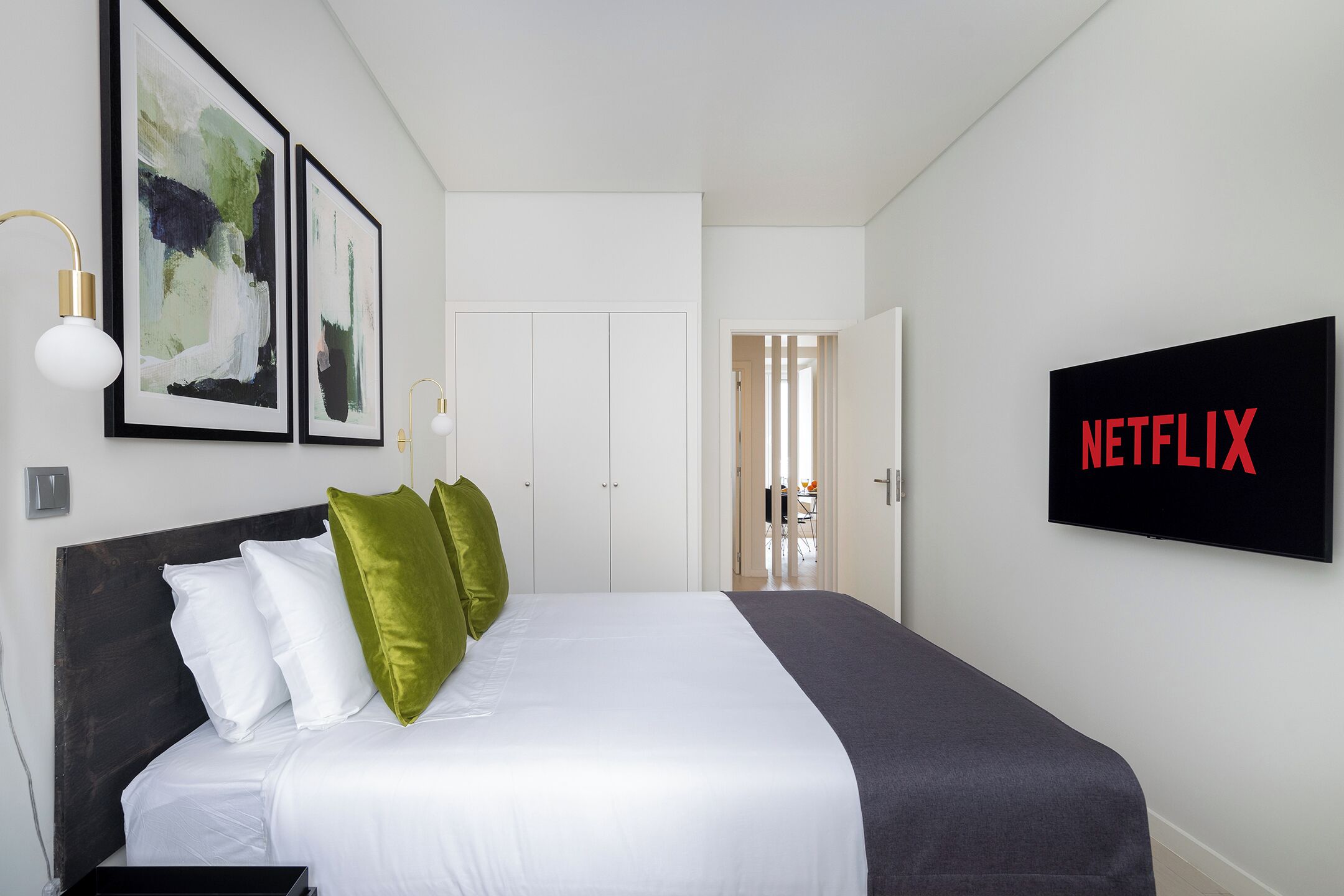 Quarto de hotel moderno com uma cama grande, uma TV exibindo 'NETFLIX' e arte abstrata emoldurada na parede.