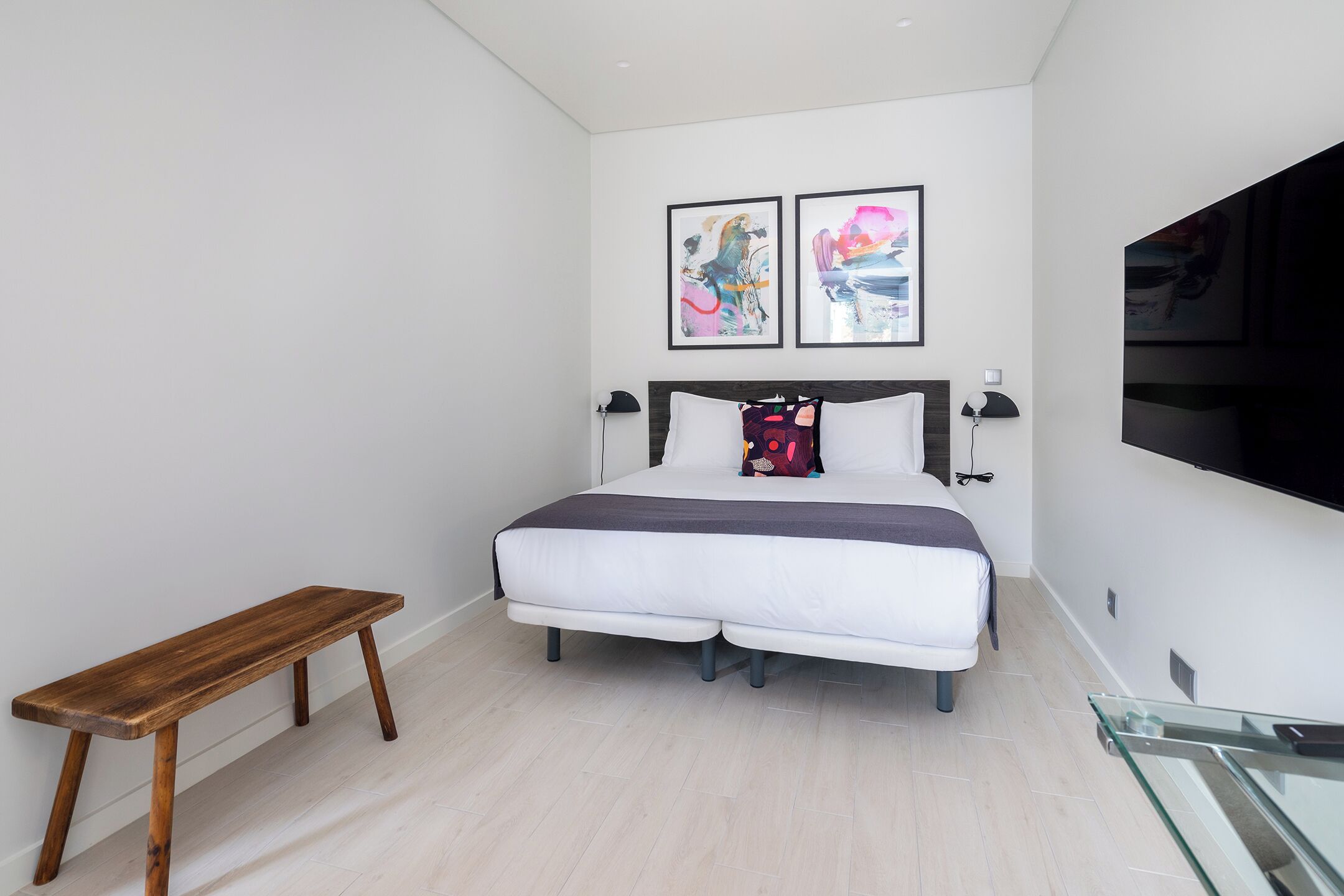 A modern bedroom with a bed, bench, and artwork on the wall.