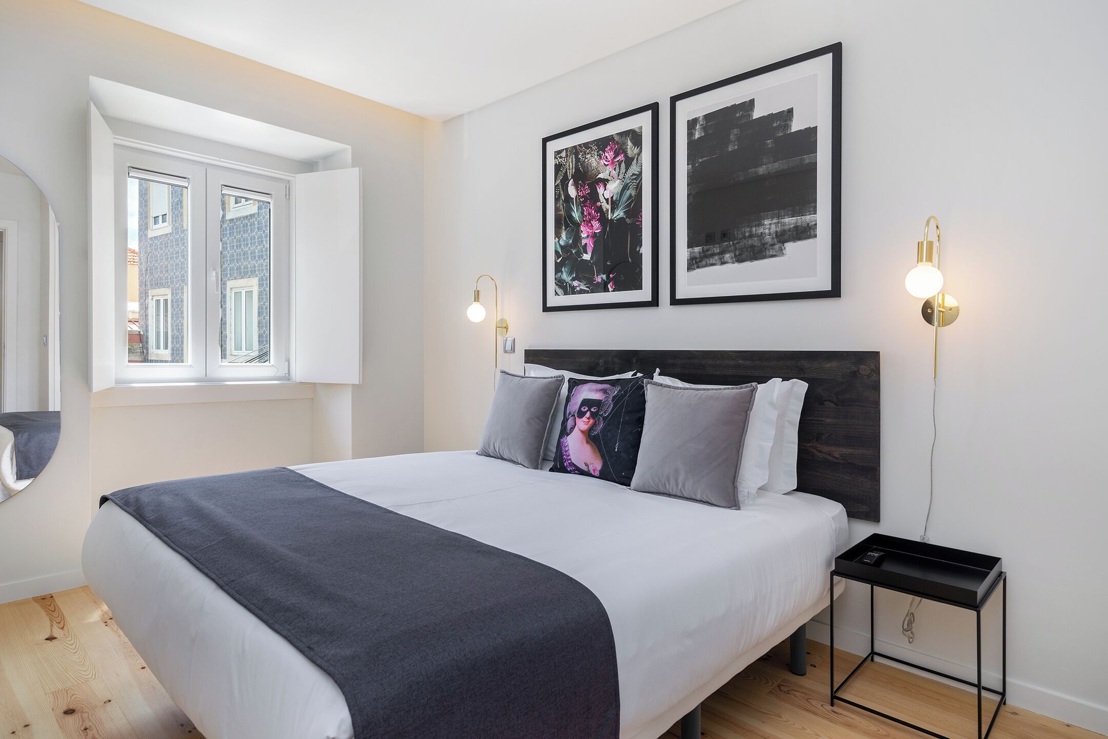A modern bedroom with a large bed, two framed artworks, bedside lamps, and a small nightstand.