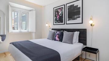 A modern bedroom with a large bed, two framed artworks, bedside lamps, and a small nightstand.
