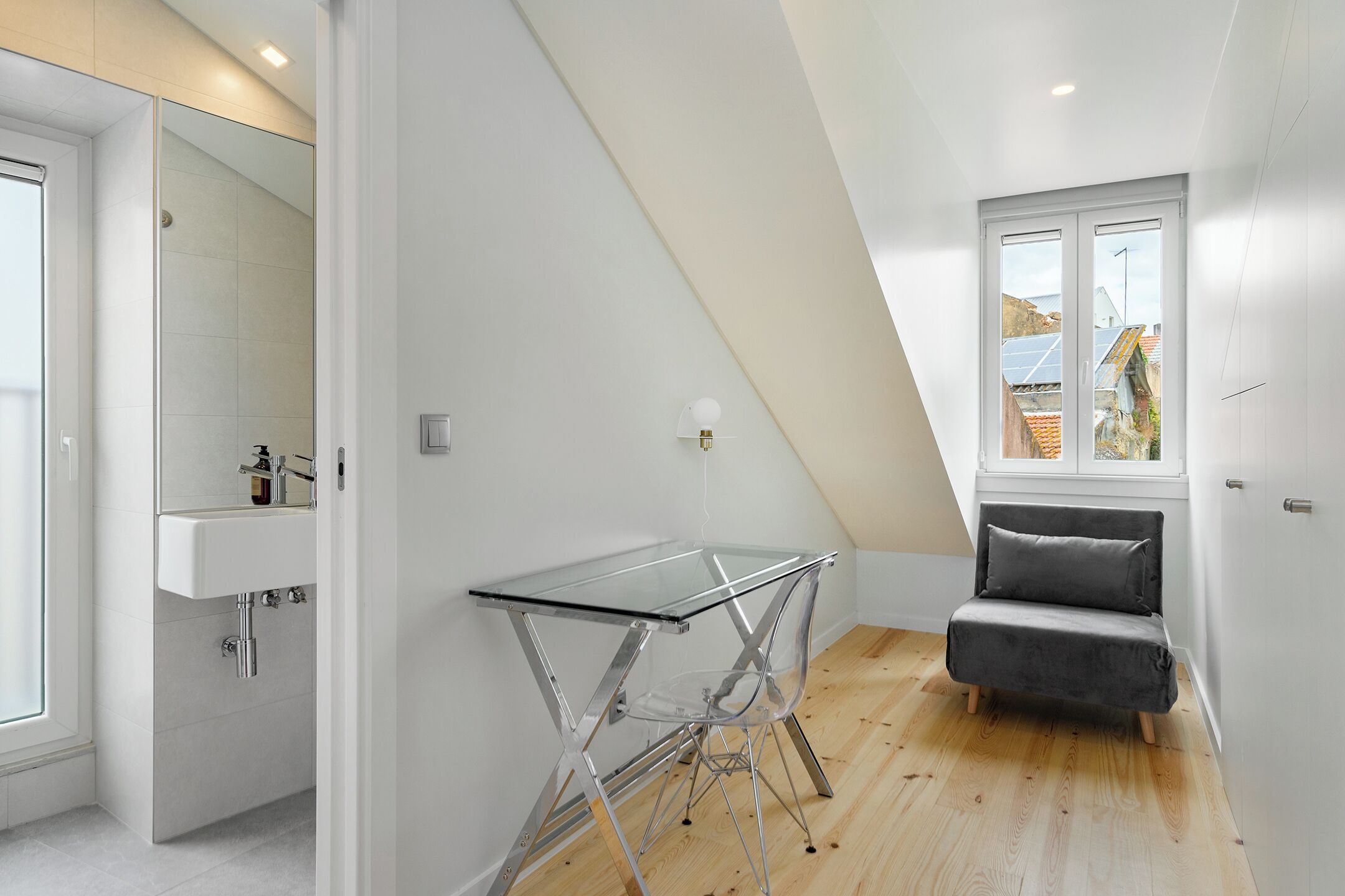 A modern, well-lit room with a glass-top table, a grey sofa, and a window with a view of buildings.
