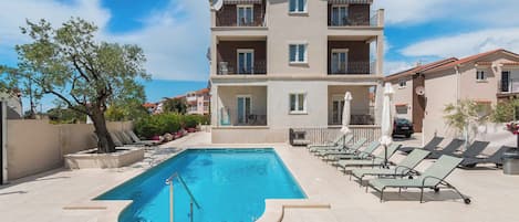 A swimming pool with lounge chairs and a building with balconies.