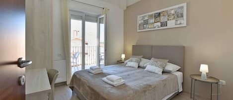 A hotel room with a bed, a chair, a table, a balcony, and a wall art piece.