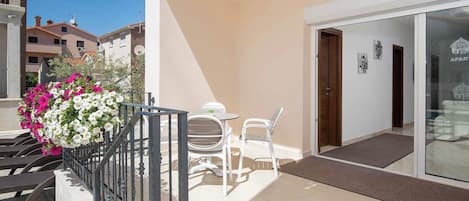 A balcony with a table and chairs, a flower arrangement, and a building entrance with a glass door.