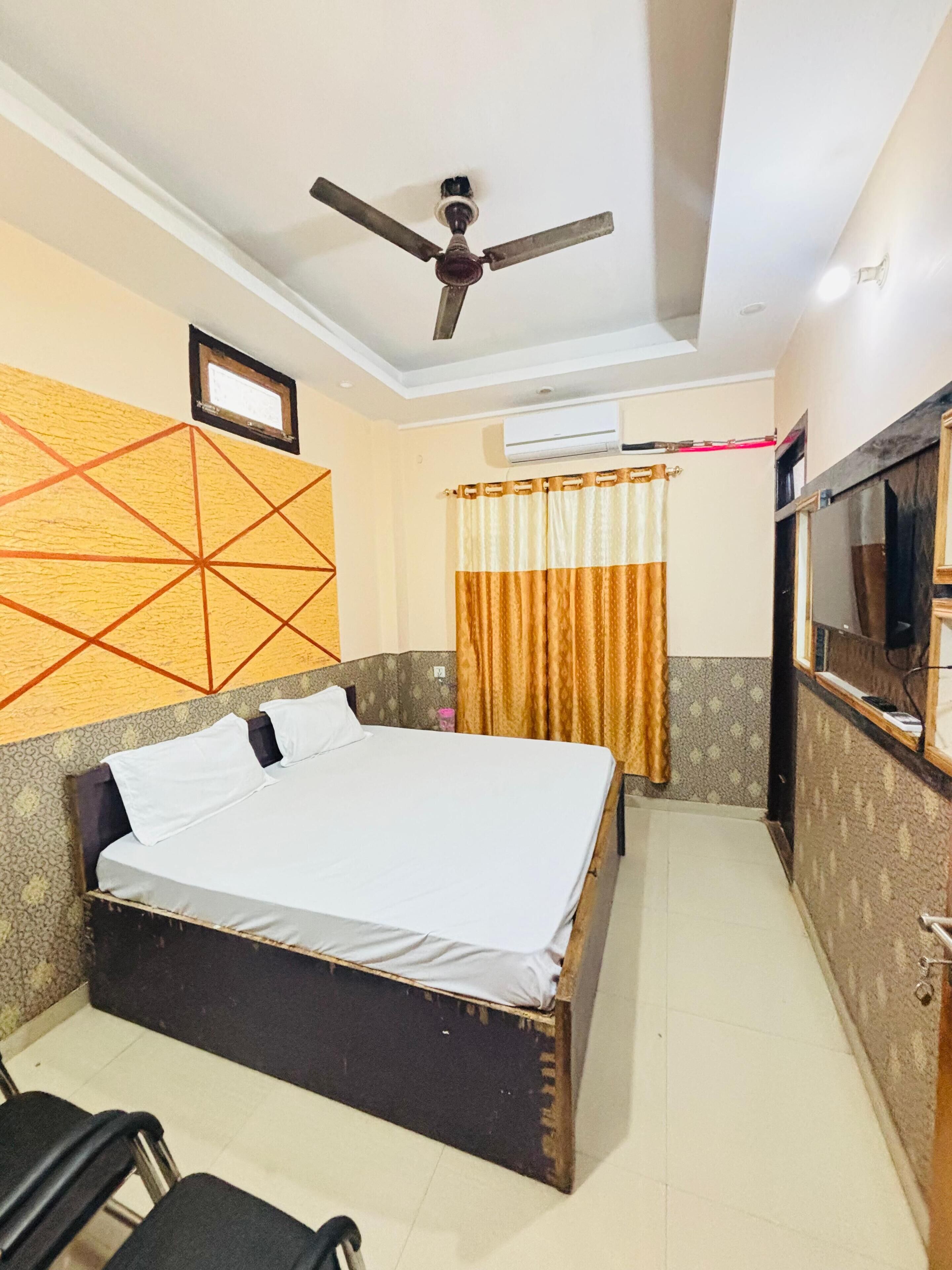 A bedroom with a bed, a ceiling fan, an air conditioning unit, a TV, and a curtain.
