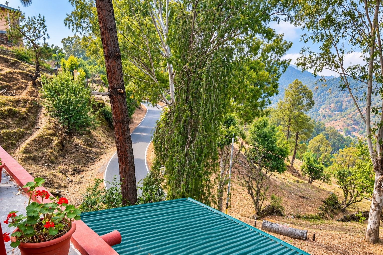 A curved road with a view of a mountainous landscape, a red railing, and a potted plant with red flowers.