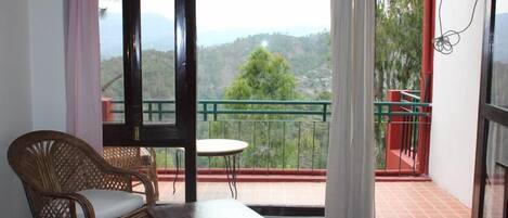 Un balcón con una silla de mimbre, una mesita y vistas a un paisaje montañoso.
