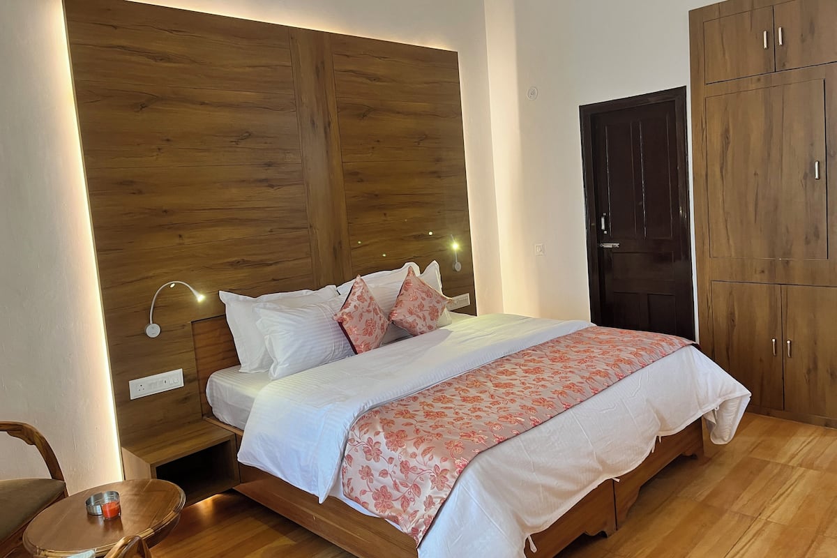 Un dormitorio con cabecera de madera, cama con ropa de cama blanca y rosa, mesita de noche con una vela y un armario.