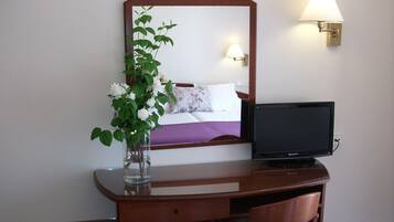 Habitación de hotel con un escritorio de madera, televisor, espejo y una lámpara fijada a la pared.