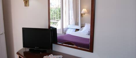 Une chambre d’hôtel avec un lit, un téléviseur posé sur un bureau en bois, un miroir et une lampe.