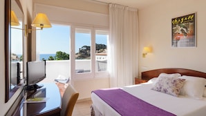 Habitación de hotel con cama, escritorio con computadora, silla y vista al mar.