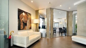 Una sala de estar moderna con un sofá blanco, un cuadro en la pared y un comedor al fondo.