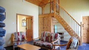 A cozy living room with two patterned armchairs, a wooden coffee table, and a staircase leading to an upper level. - Griffins Holiday Cottage (Murreagh)