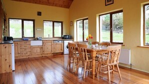 A spacious kitchen with wooden cabinets and a dining area with a table and chairs. - Griffins Holiday Cottage (Murreagh)