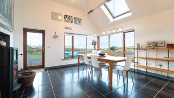 A spacious kitchen with a large dining table, modern appliances, and large windows offering a view of the outdoors.