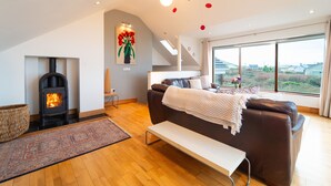 A modern living room with a fireplace, a sofa, a bench, and a large window offering a view of the outdoors. - Great Blasket, Dunquin (Dunquin)