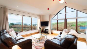 A spacious living room with leather sofas, a glass coffee table, and a large TV.