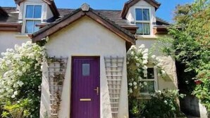 A house with a purple door, a small porch, and potted plants. - Orchard Cottage - Dingle (Dingle)